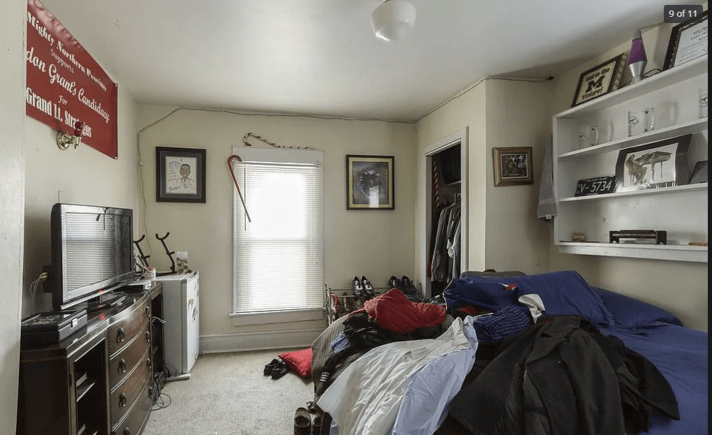 A bedroom with a bed, dresser, and a window with blinds.