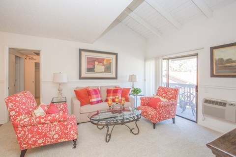 A living room with a red floral patterned chair and a glass coffee table.