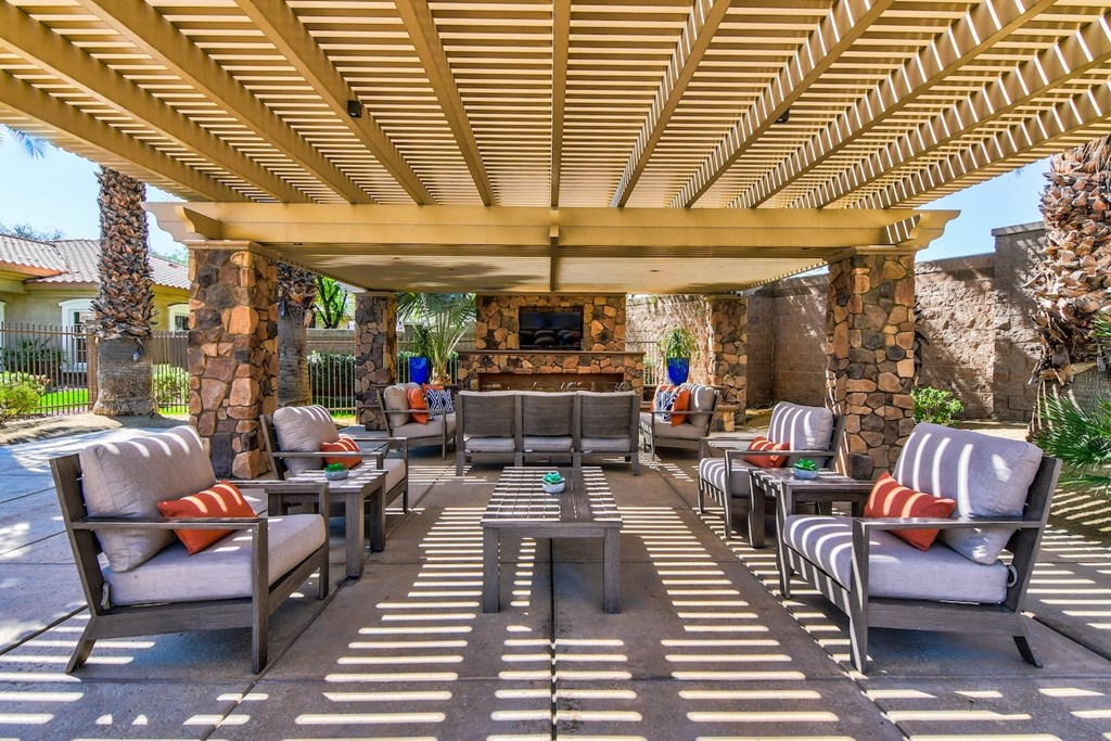 A patio with a stone fireplace and a wooden pergola.