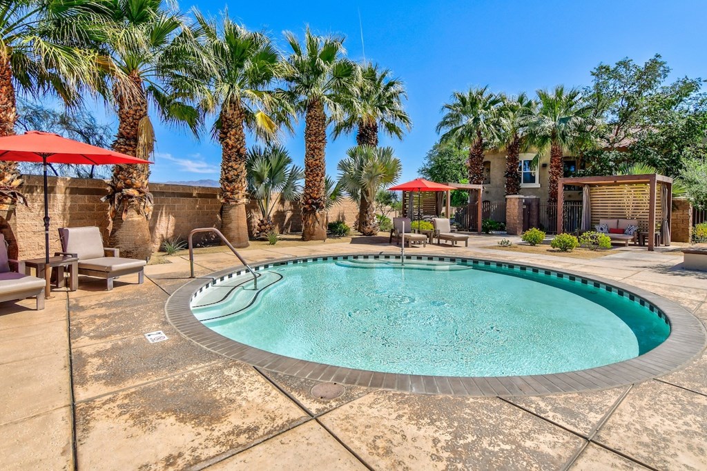 A pool surrounded by palm trees and a patio area with chairs and umbrellas.