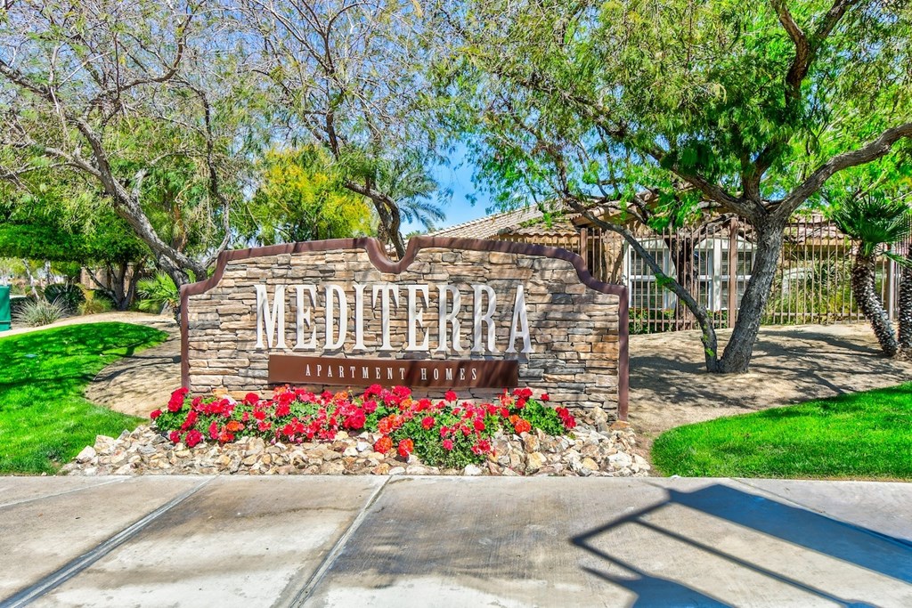 The entrance to Mediterra Apartments is surrounded by red flowers and greenery.