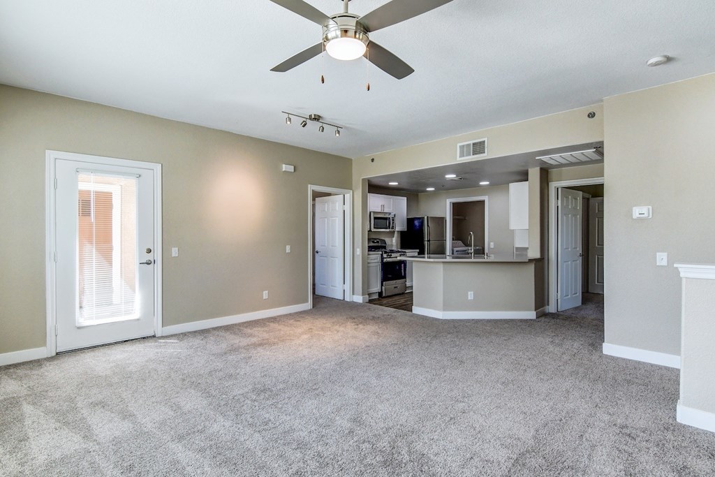 A spacious living room with a ceiling fan and a kitchen area in the background.