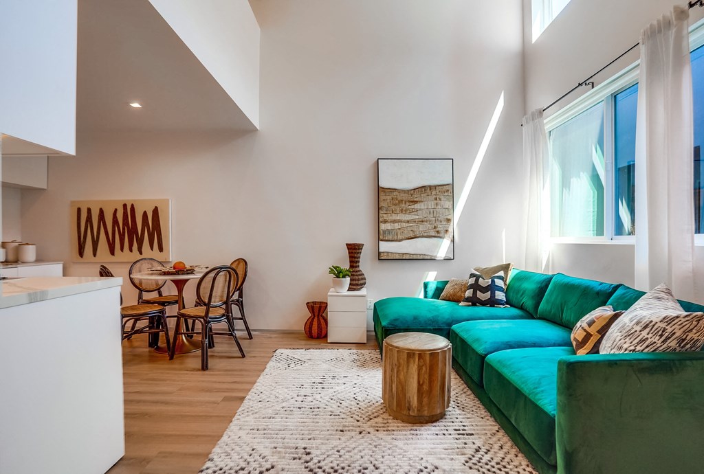 a living room with a green couch and a white kitchen with a dining table and chairs