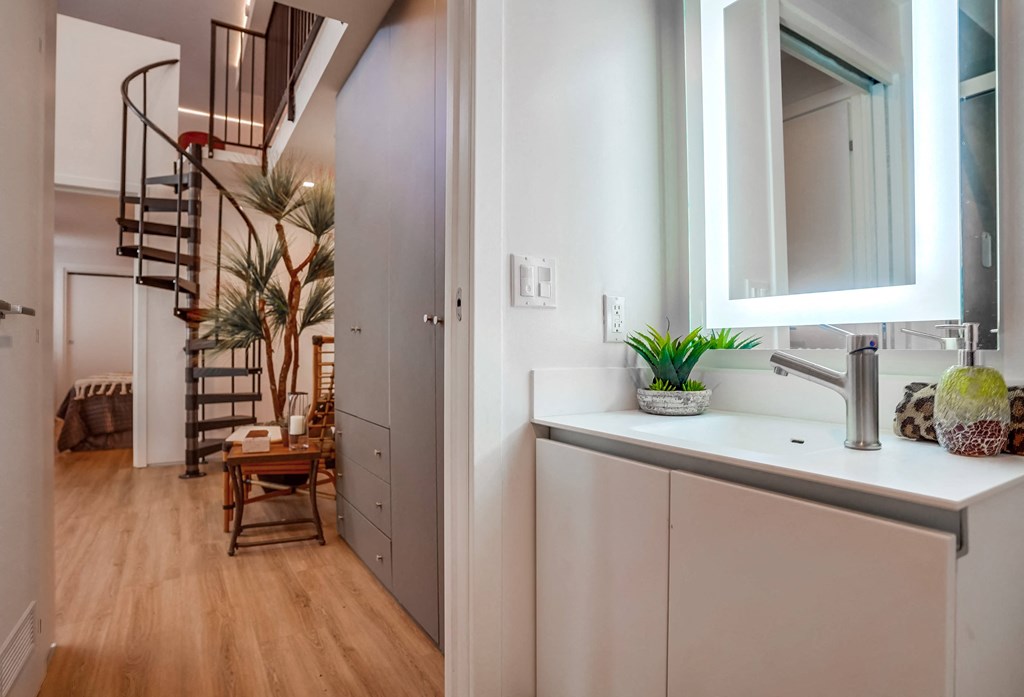 a small bathroom with a sink and mirror and a spiral staircase in the background