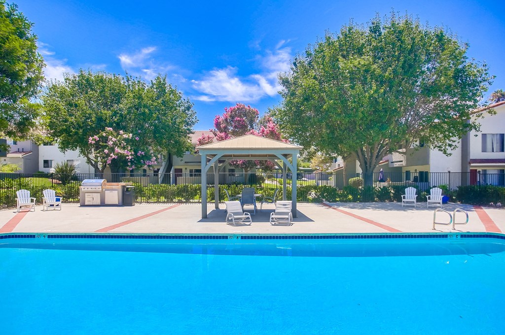 a swimming pool with chairs and a gazebo in front of a building
