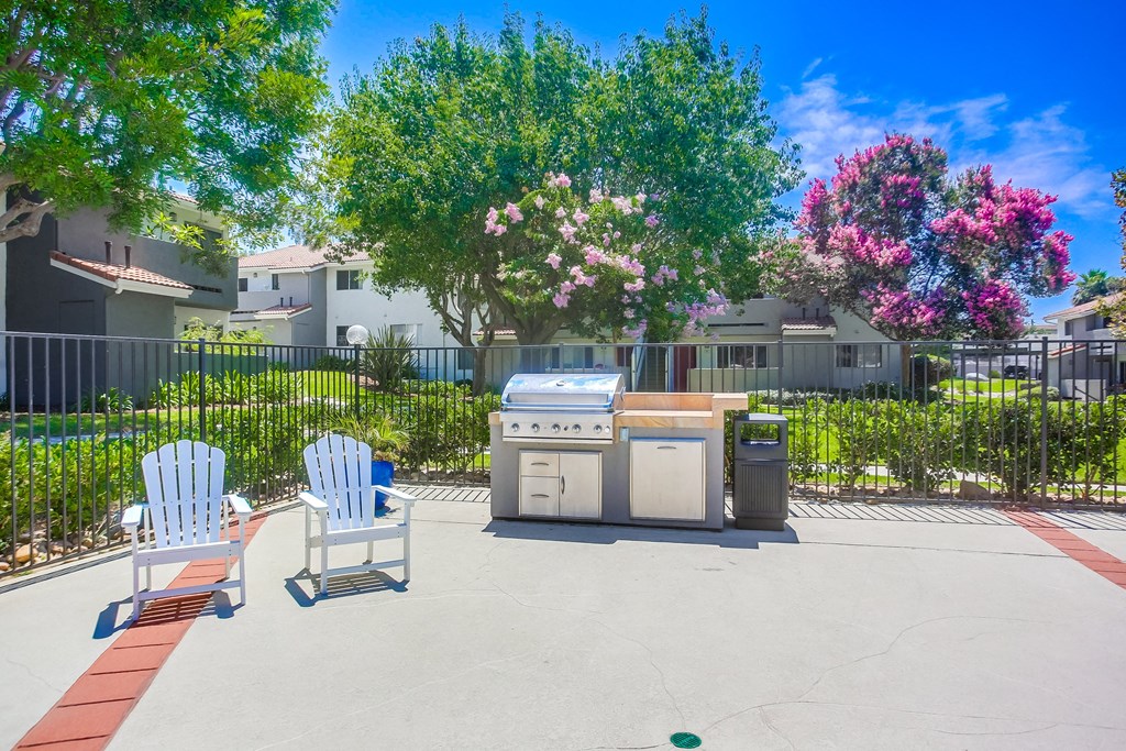 a patio with two chairs and a grill in front of some trees