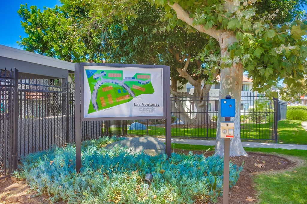 a sign in front of a park with a tree and a fence
