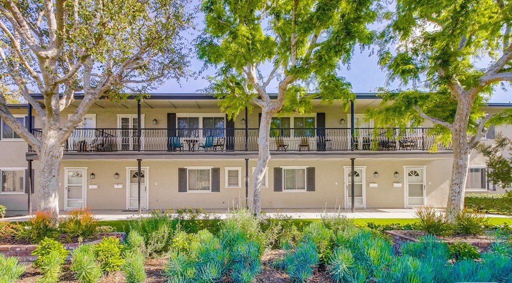 A row of apartments with balconies and trees in front.