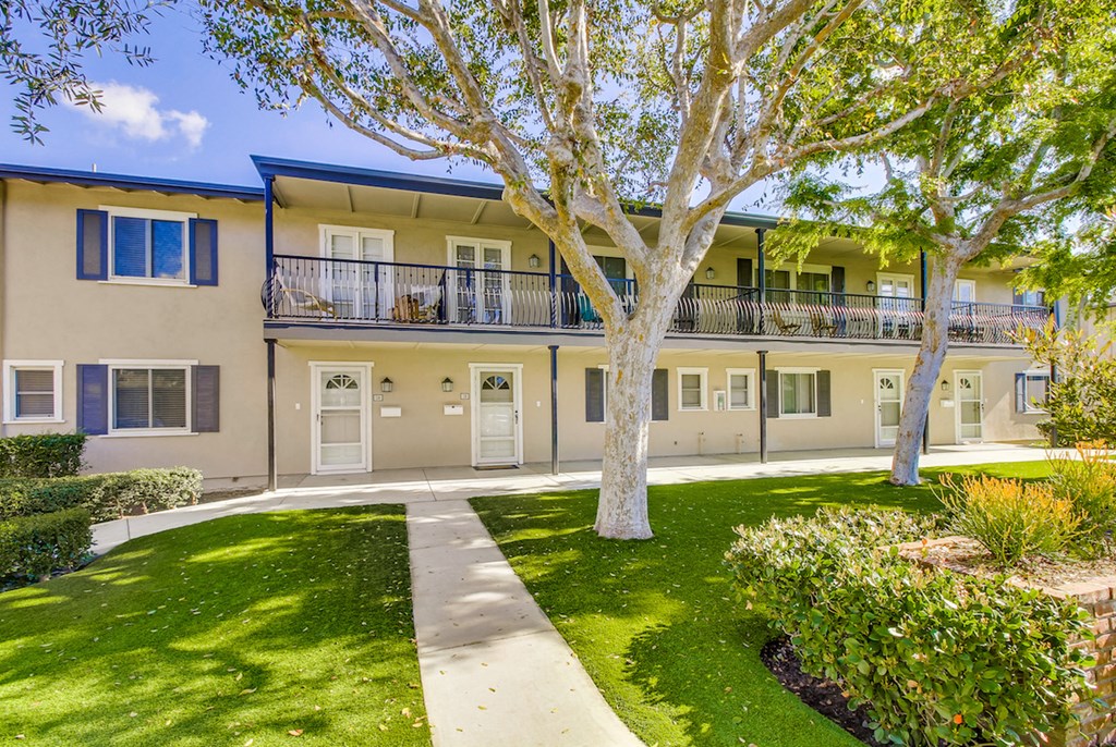 An apartment with a balcony and a tree in front.