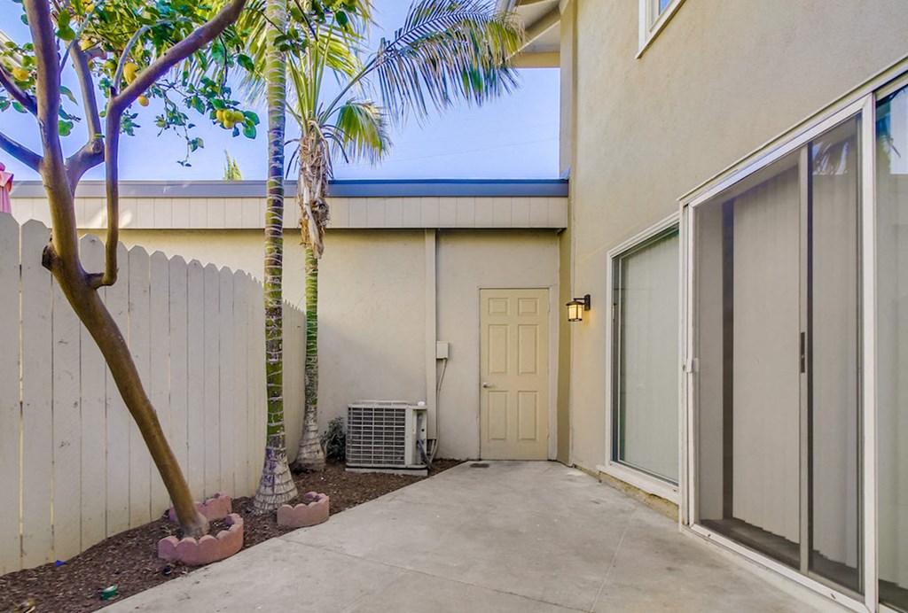A tree in a pot is in front of a white fence.