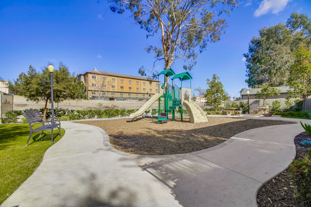 A playground with a green slide and a concrete walkway.