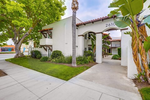 A white house with a red tile roof and a palm tree in front.