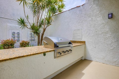 A wall-mounted grill is on a patio with a tree and a sign.