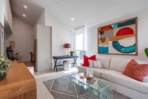 A modern living room with a white sofa and a colorful abstract painting on the wall.