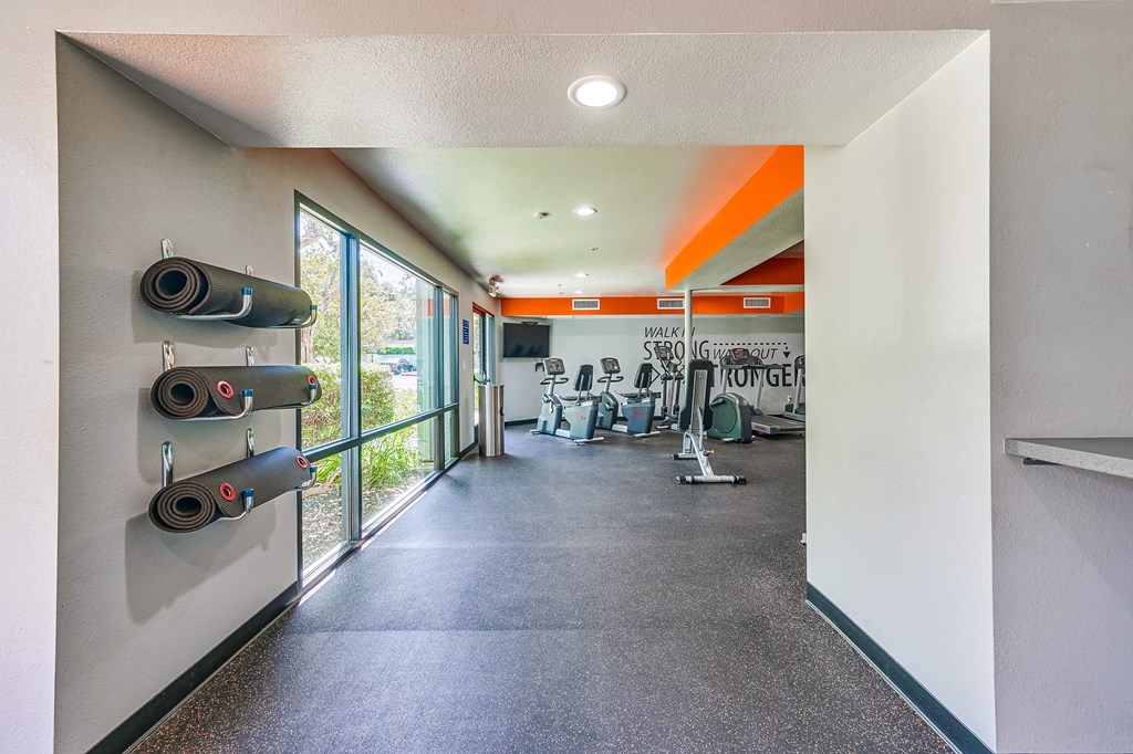 a fitness room with a treadmill and weights on the wall