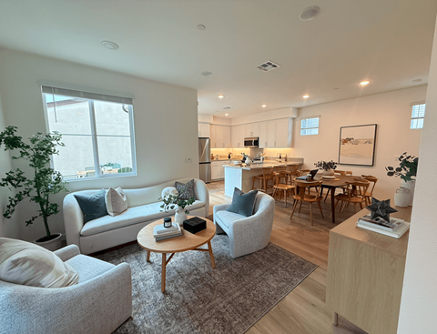 A living room with a grey couch, a wooden table, and a dining table with chairs.