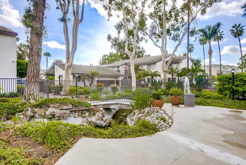 a garden with a bridge and palm trees in front of a house