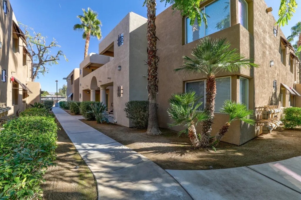 a sidewalk in front of a building with palm trees