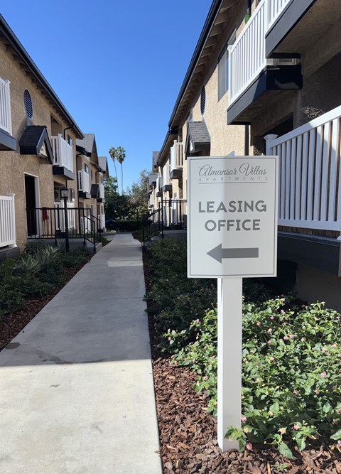 A sign for a leasing office is on the right side of a walkway.
