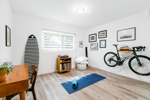 A room with a surfboard, a bicycle, and a dining table.