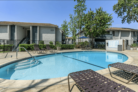 A pool with a slide and sun loungers in front of apartment buildings.