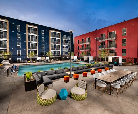 A poolside area with a table and chairs and two buildings in the background.