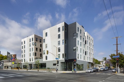 A modern building with a white and grey exterior is situated on a street corner with cars and traffic lights.