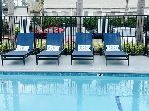 Four lounge chairs with the word "POOL" on them are arranged in a row by a pool.