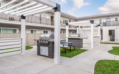 A patio with a grill and picnic table is surrounded by white balconies.