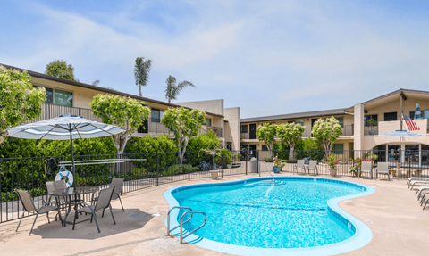 A swimming pool surrounded by chairs and umbrellas in front of a building.