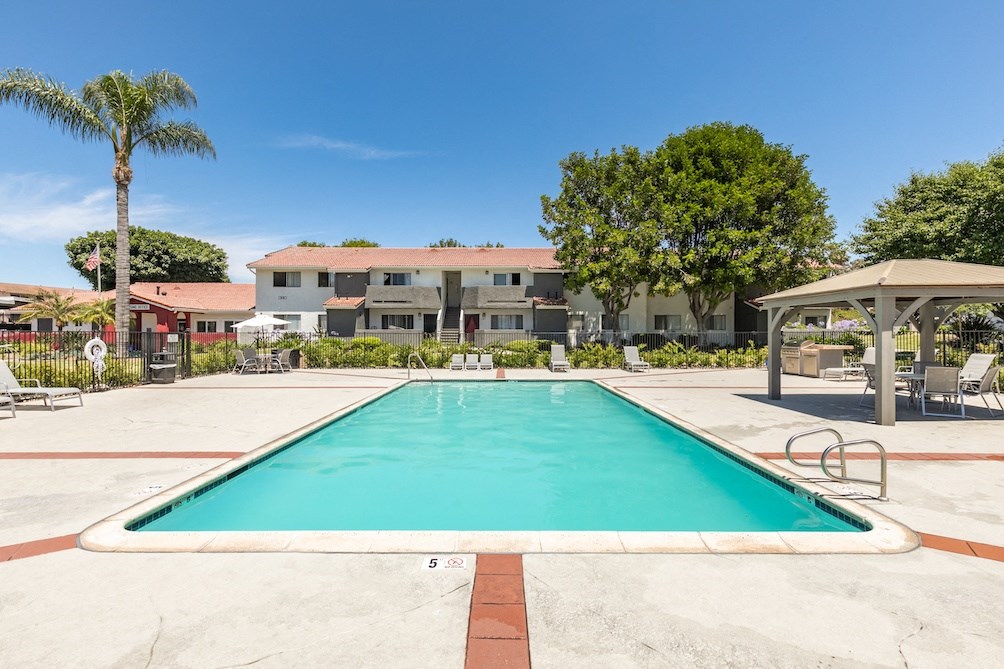 a swimming pool with a gazebo and apartment buildings in the background