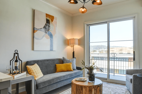 A living room with a grey couch, a table with a lamp and a painting on the wall.