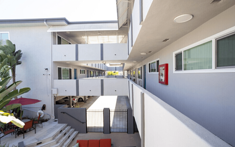 A white building with a red umbrella and a red bench.