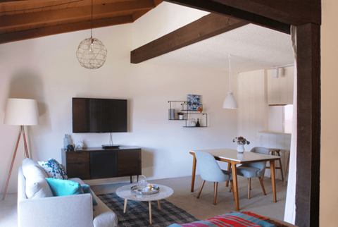 A living room with a white couch, a wooden coffee table, and a television on the wall.
