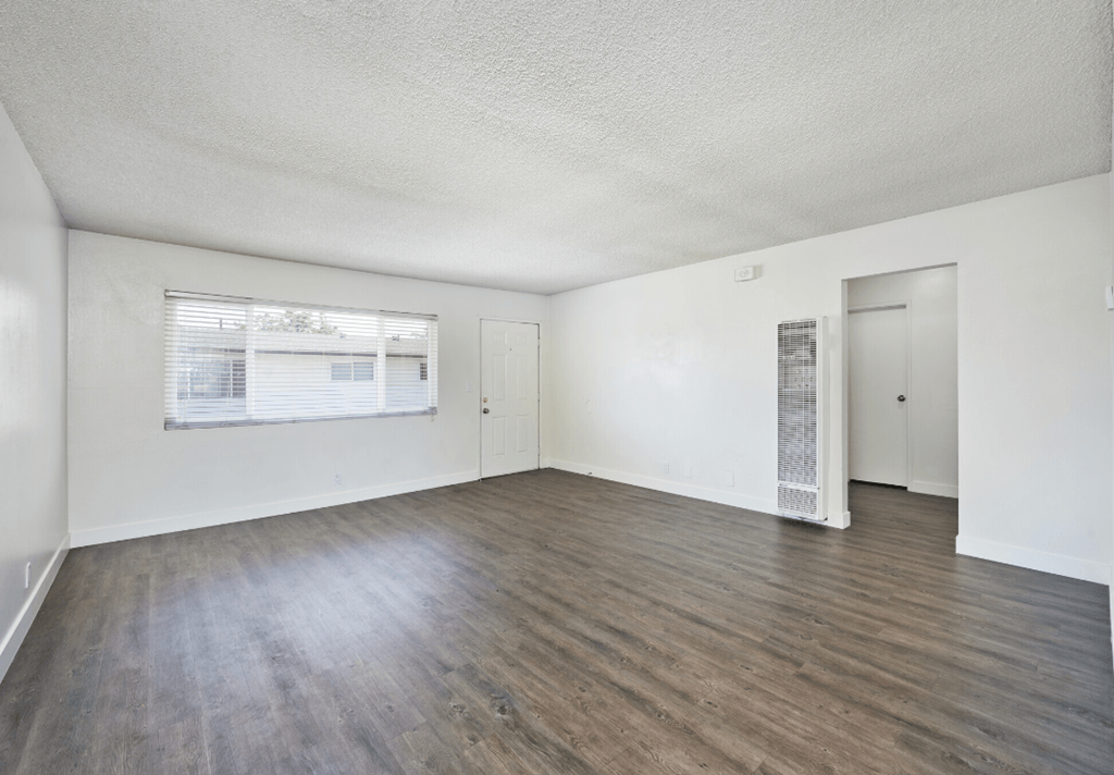 the living room of an apartment with wood flooring and a window