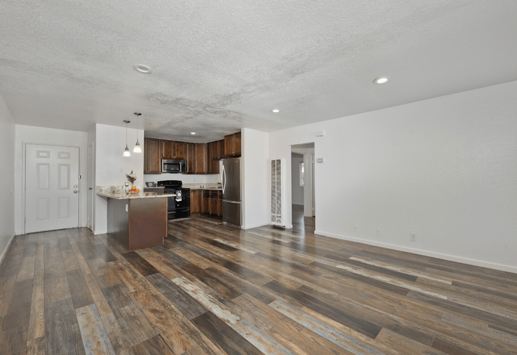 the living room and kitchen of an apartment with wooden floors and white walls