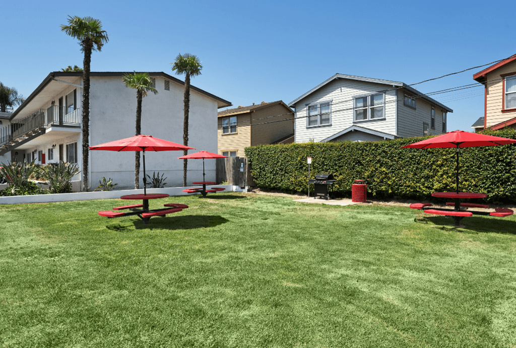 a backyard with picnic tables and umbrellas in front of houses