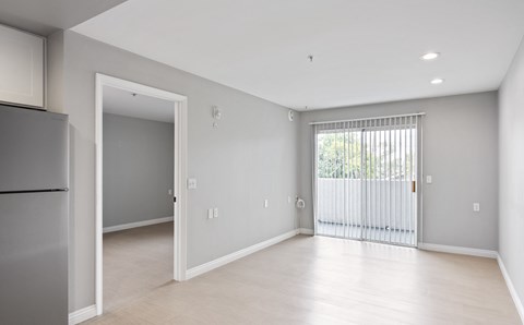A spacious, empty room with a refrigerator on the left and a sliding glass door on the right.