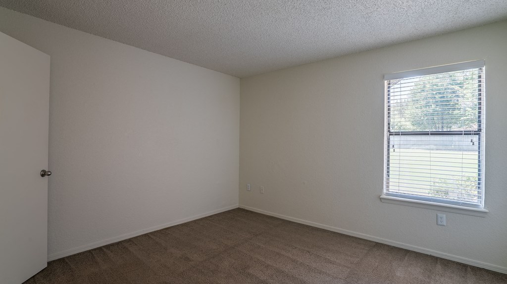 an empty bedroom with a window and a wooden floor