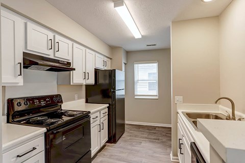 A kitchen with a black stove top oven, black refrigerator, and white cabinets.