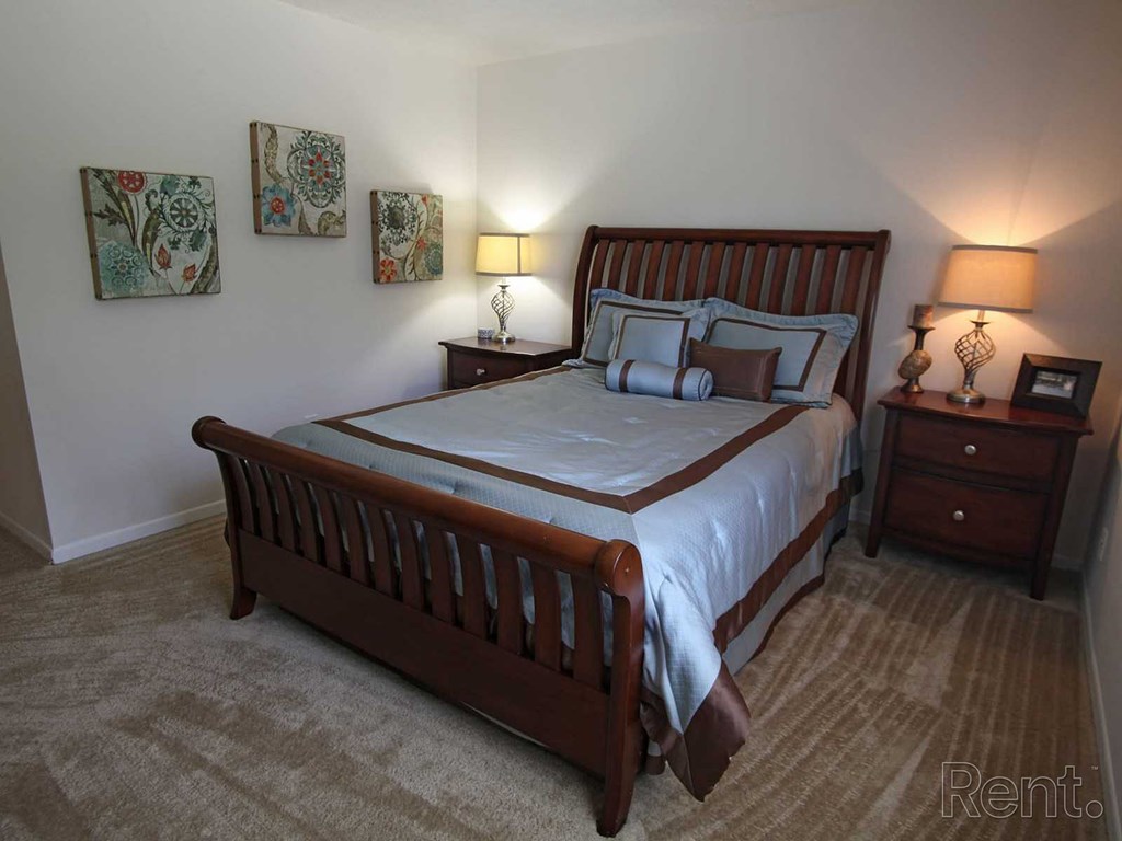 A bedroom with a large bed, two lamps, and two pictures on the wall.