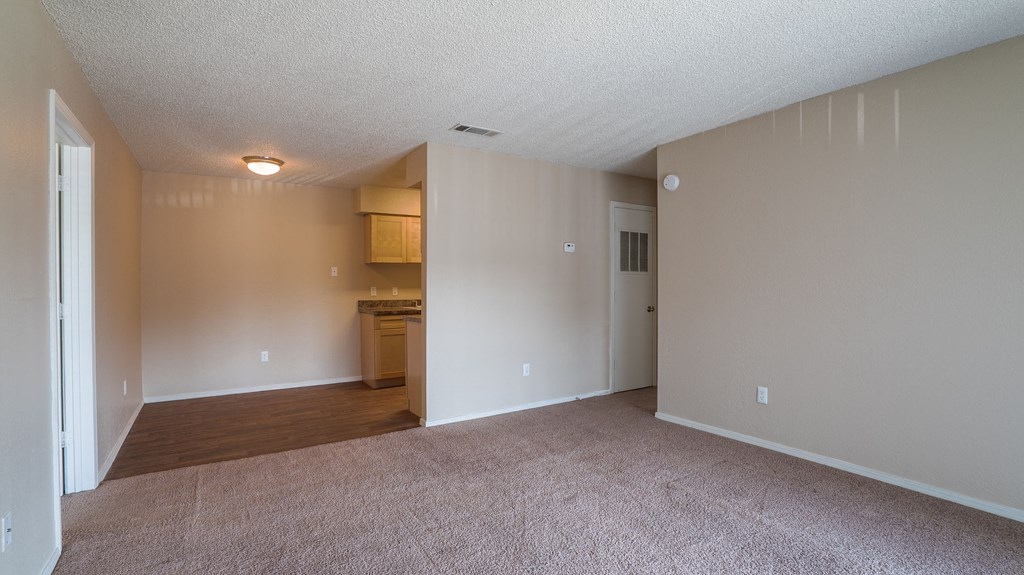 an empty living room with a kitchen in the background