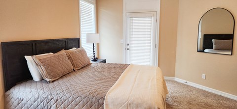 A bedroom with a bed, lamp, and mirror.