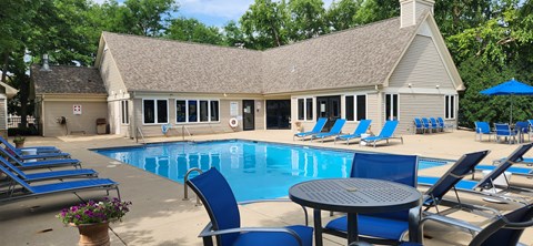 A pool with blue chairs and a table in front of a house.