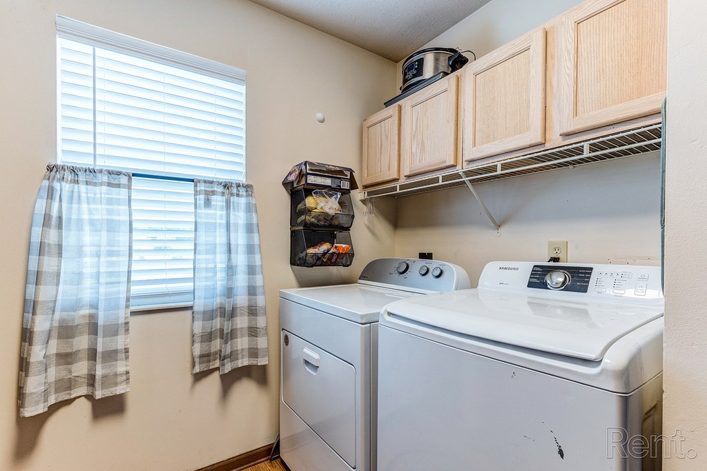 a laundry room with a washer and dryer and wood cabinets and a window