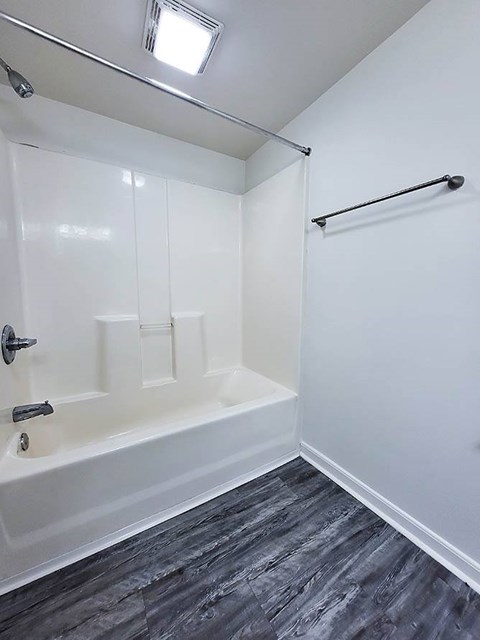 A white bathroom with a tub and a grab bar.