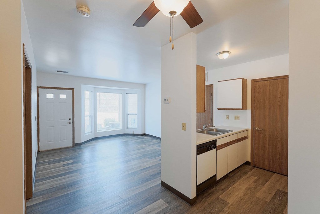 an empty living room and kitchen with wood flooring and a ceiling fan