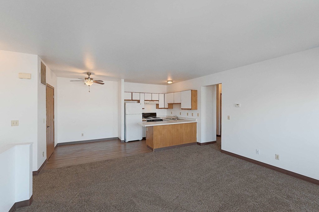 an empty living room with a kitchen and a ceiling fan