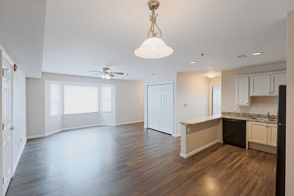 an empty living room and kitchen with wood flooring and a ceiling fan
