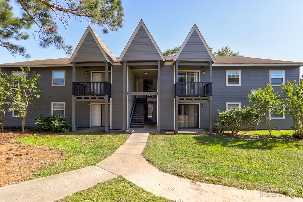 a gray apartment building with three peaked roofs and a sidewalk